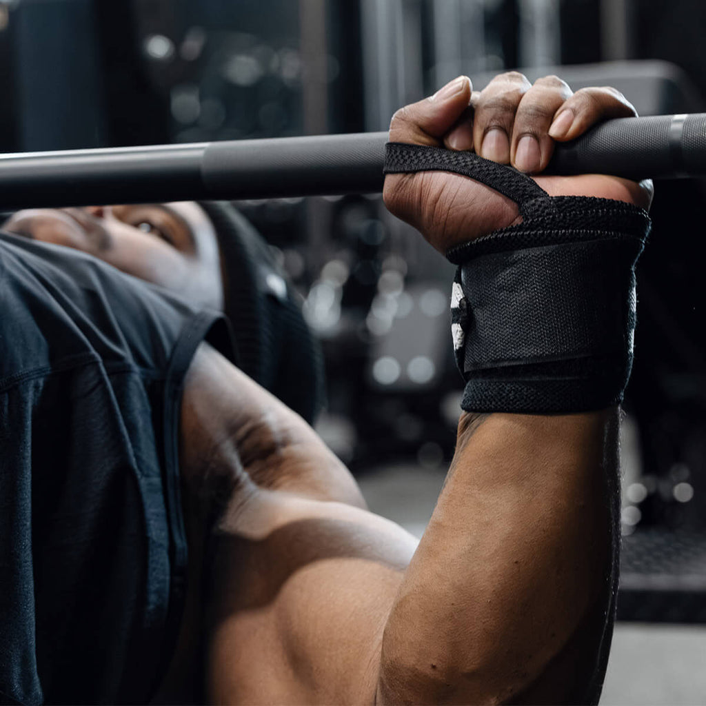 IFBB Pro bodybuilder executing a powerful bench press at the gym, showcasing Gymreapers premium wrist wraps for optimal wrist support and stability. The athlete's muscular build and controlled form highlight the wrist wraps’ durability, perfect for heavy lifting sessions to maximize performance and reduce strain. Gymreapers wrist wraps provide unparalleled support, ideal for weightlifting enthusiasts and professionals aiming for superior results in pressing movements like the bench press. Fitness gear designed by athletes, for athletes, to elevate every lift.