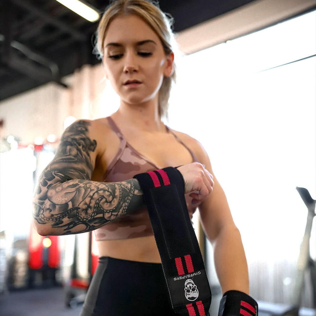 Female athlete tightening Gymreapers wrist wraps at the gym, preparing for a strength training session. The wrist wraps offer support and stability, ideal for weightlifting and enhancing grip strength. Gymreapers gear is designed to boost performance and reduce injury, helping athletes lift with confidence and focus on their goals.